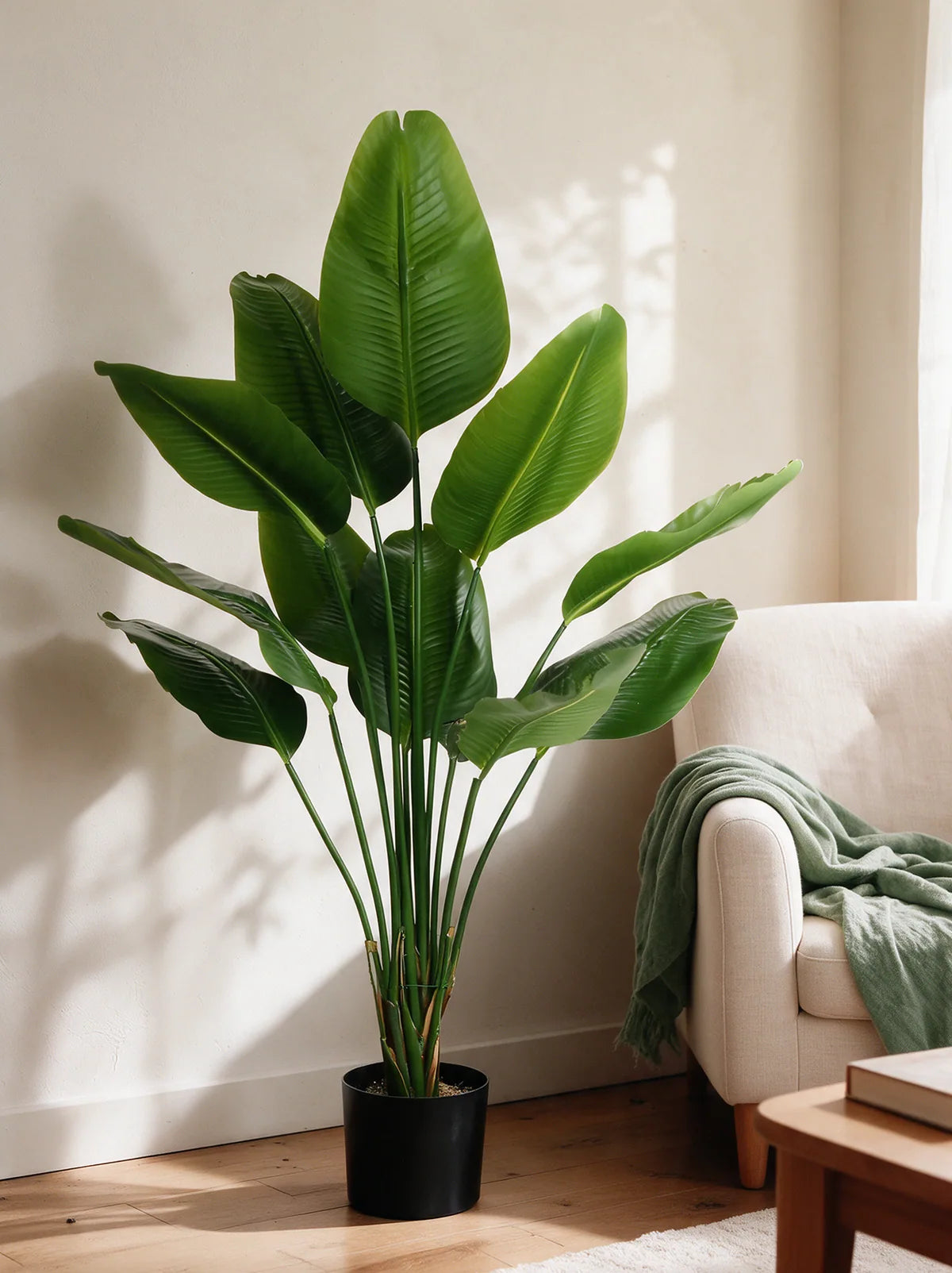 En naturtro Strelitzia ved en lys lenestol med et grønt pledd.